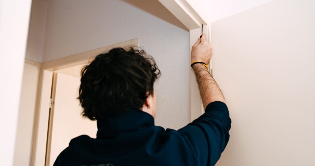 Technicien BTP Diagnostics effectuant un prélèvement au moyen de lingettes sur un encadrement de porte dans le cadre d’un diagnostic plomb